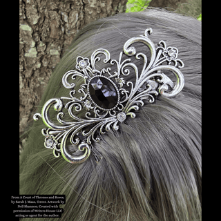 Silver hair comb with intricate floral and swirl details, featuring a black gemstone centerpiece, styled in silver-gray hair against a natural tree backdrop.