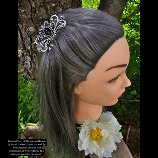 Silver hair comb with intricate floral and swirl details, featuring a black gemstone centerpiece, styled in silver-gray hair against a natural tree backdrop.