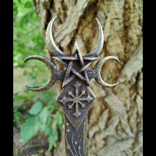 A bronze-colored dagger-shaped hair stick featuring intricate designs inspired by the Goddess Nyx. The top portion showcases crescent moons and a pentagram interwoven with a gothic cross, symbolizing the mysteries of the night. The shaft is adorned with cascading shooting star patterns, enhancing its celestial theme.