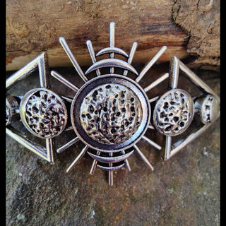 A close-up shot captures the central detail of the comb—a hammered-texture lunar sphere, surrounded by radiating lines and smaller lunar shapes. The craftsmanship is accentuated against the natural backdrop of a rustic wooden branch.