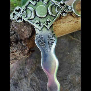 A detailed shot of the hair dagger’s handle, highlighting two engraved torches and a crescent moon motif surrounded by intricate patterns against a rustic wooden background.