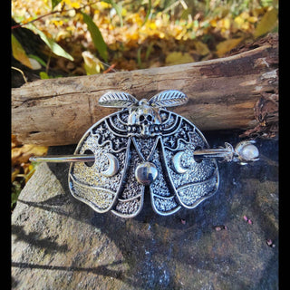 Death moth hair cage styled with a pearl-tipped hairpin inserted, laid on a natural stone surface.