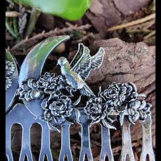 A detailed view of the hair comb's crescent moon design, adorned with a bird in mid-flight and blooming flowers. The intricate craftsmanship highlights its whimsical and naturalistic charm