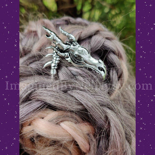 The dragon skull hair scythe displayed in a braided updo, emphasizing its fantasy aesthetic with a background of lush greenery