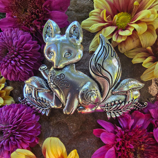 Silver fox-shaped hair barrette surrounded by vibrant pink, purple, and yellow chrysanthemums, displayed on a textured stone background to emphasize the intricate engraved details and metallic finish