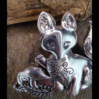 Close-up view of a silver fox hair barrette, showcasing the fox's intricately engraved face, including its pointed ears, detailed eyes, and engraved swirl patterns, against a rustic stone background