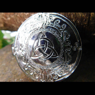 A front-facing view of the silver locket showcasing its intricate triquetra design. The detailed scrolling motifs around the symbol are deeply etched, creating contrast against the polished silver finish. The natural bark background enhances the rustic aesthetic of the piece.