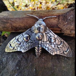 A frontal view of the silver moth hair clip on a natural wood background. The eye-shaped motif on the moth’s head and the intricate lunar details on the wings are highlighted, creating a striking celestial-inspired aesthetic.