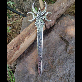 The full view of the Nyx-inspired hair dagger resting against a wooden background. The elongated blade, adorned with celestial carvings, culminates in the crescent moons and pentagram at the top, creating a powerful tribute to the goddess of night.