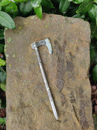 Detailed close-up of a silver Viking hatchet hair stick featuring Celtic knot engravings, photographed on a stone surface