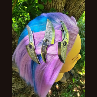 multiple knife-shaped hair clips, layered stylishly on vibrant pink and blue hair. The clips’ sharp, metallic details stand out as bold fashion accessories