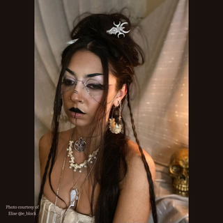 A styled shot featuring the Nyx hair dagger in a model’s hair. The gothic aesthetic of the hair stick complements the model's dark makeup and elaborate braided hairstyle, reinforcing its ethereal and mysterious appeal.