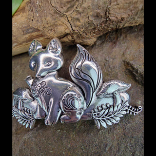 Full view of a silver fox-shaped hair barrette with flowing tail and engraved floral patterns, displayed on a rough stone surface that enhances the intricate metal craftsmanship