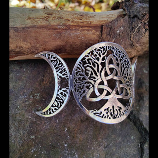 Perspective view highlighting the intricate tree and crescent moon design, propped against a wooden log on a stone surface