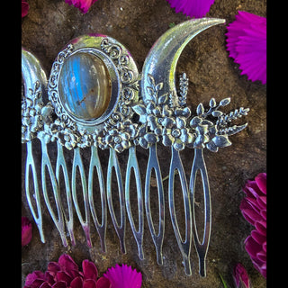 Close-up of the silver hair comb resting on a rock, focusing on the crescent moon and floral details on the right side. The image captures the delicate engravings and metallic shine, contrasting beautifully with the textured natural background