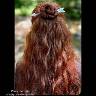 Silver arrow-shaped hair stick securing a twisted bun in long red hair, styled in a natural outdoor setting