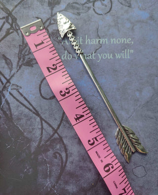 Silver arrow-shaped hair stick with engraved arrowhead and feather details, displayed on a decorative background with a pink measuring tape for size reference