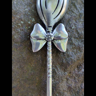 Close-up of the bow detail on a silver broom hair stick, featuring a pentagram engraving and intricate textures, displayed on a stone surface