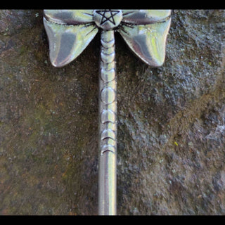 Close-up of the handle of a silver broom hair stick, showing engraved moon phases and textured details, displayed on a natural background