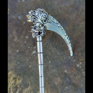 A highly detailed silver hair scythe inspired by Santa Muerte, featuring an intricate floral design along the blade and handle. The scythe's blade curves gracefully, adorned with ornate patterns, while the top displays a menacing skull encased in decorative engravings. The scythe handle mimics a segmented rod, emphasizing the weapon's grim aesthetic, and rests on a textured stone background.