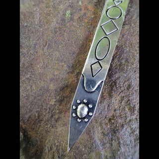 A detailed close-up of the tip of the Persephone-inspired hair dagger. The silver blade features engraved geometric shapes—diamonds, ovals, and circles—paired with a crescent moon and a sunburst detail around a central gemstone. The metal finish is slightly antiqued, highlighting the depth of its craftsmanship.