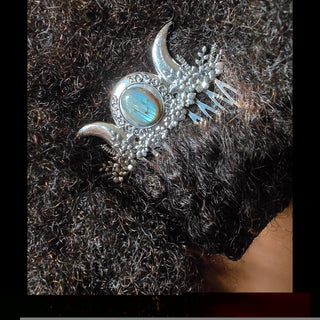 A silver hair comb with crescent moon accents and a labradorite centerpiece styled in textured black curls. The comb's floral detailing stands out against the voluminous curls, emphasizing the mystical and earthy aesthetic