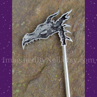 underside of a highly detailed silver dragon skull hair scythe shown on a rock surface, highlighting its intricate skeletal design and sharp curved blade