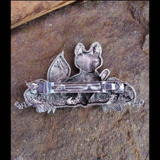 The back of a silver fox-shaped hair barrette, featuring a sturdy metal clasp and fine detailing, displayed on a rugged stone background with natural texture