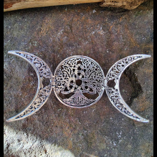 An underside view of silver hair clip featuring a Tree of Life design, flanked by crescent moons on either side, placed on a textured stone surface