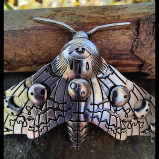 A close-up of the silver moth hair clip reveals its ornate central motif, an eye-like design at the moth’s head. The wings are adorned with crescent moons and intricate linear patterns, giving the accessory an ethereal and mystical look.