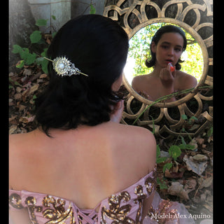 Crescent moon hair stick styled in short, dark hair, worn by a model in an elegant pink dress with golden embroidery, reflected in a decorative mirror outdoors, framed by fallen leaves and tree trunks. model: Alex Aquino